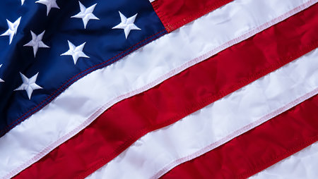 A detailed close-up shot of an American flag, showcasing the intricate texture of the fabric and the embroidered white stars on a deep blue field. The image emphasizes the red and white stripes, their subtle folds, and the delicate stitching that defines each stripe.  The colors are vibrant and saturated, offering a rich visual experience. The composition focuses on the texture and detail of the flag's material, creating a tactile and patriotic feel.の写真素材