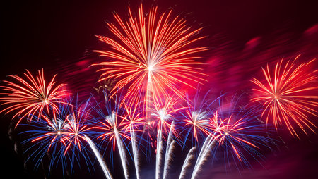 A vibrant display of red and blue fireworks against a dark night sky. Multiple fireworks burst outwards, creating streaks of light and color. The image captures the dynamic energy and excitement of a fireworks show, with a focus on the contrasting colors and intricate patterns of the explosions. The overall mood is celebratory and festive.  The colors are intensely saturated, with deep reds and bright blues dominating the scene.  The fireworks appear to be at various stages of their burst, some fully expanded, others still ascending.の写真素材