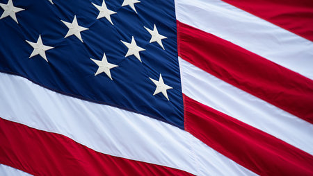 A close-up shot of a portion of an American flag. The image focuses on the detail of the stars and stripes, showcasing the texture and folds of the fabric.  The colors are vibrant: deep blue canton with off-white stars, alternating red and white stripes. The flag appears to be waving gently, creating soft folds and creases in the material. The focus is sharp on the stars and the immediate surrounding area, with a slight softness towards the edges. The overall mood is one of solemnity and patriotism.の写真素材