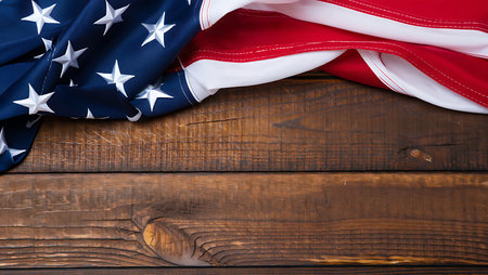 A portion of an American flag is draped over a dark brown wooden surface. The flag's deep blue field with white stars and red and white stripes are visible. The wood planks have a rustic texture with visible grain and knots. The image is composed with the flag in the upper left corner, leaving a significant portion of the wooden background visible. The overall mood is patriotic and slightly rustic.の写真素材