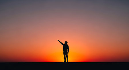 Silhouette of a man standing on top of the hill and looking at the sunsetの写真素材