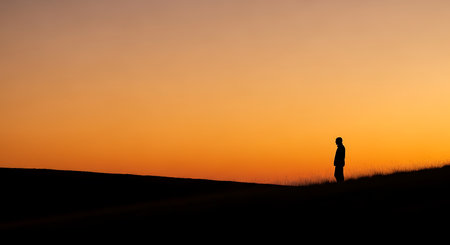 Silhouette of a man standing on a hill at sunset.の写真素材
