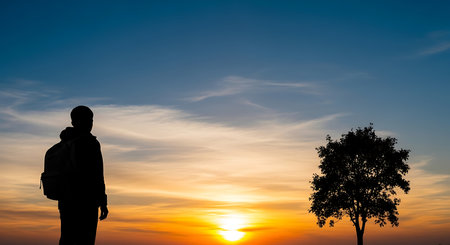 Silhouette of a man with a backpack on the background of the sunsetの写真素材