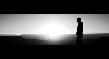 Silhouette of a man standing on the edge of a cliff and looking at the sunsetの写真素材
