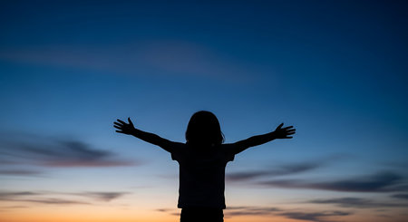 Silhouette of a girl with open arms against the sunset skyの写真素材