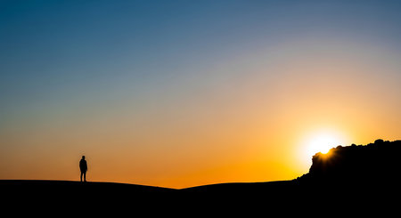Silhouette of a man standing on top of a hill during the sunset.の写真素材