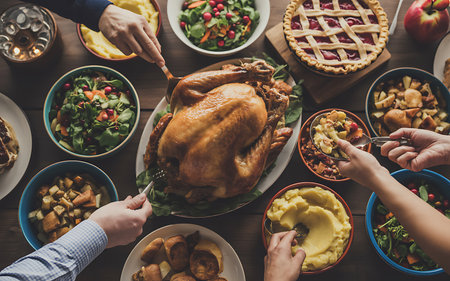 Overhead shot of a Thanksgiving or Christmas feast with a large roasted turkey as the centerpiece surrounded by bowls of sides salads mashed potatoes stuffing and desserts like pie with multiple hands reaching in to serve themselves from the spread of food for a celebratory meal with family and friendsの写真素材