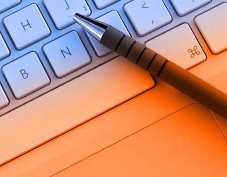 Pen resting on laptop keyboard with orange lighting effectの写真素材