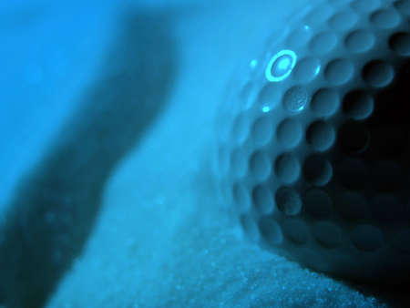 Close-up of golf ball in sand with blue ighting effectの写真素材