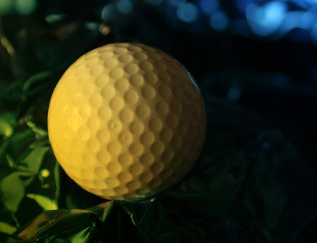 Close up of golf ball on crumpled foil with yellow lighting effectの写真素材