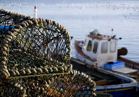 Stacked lobster baskets with out of focus fishing boatsの写真素材