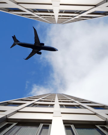 Office block agaist cloudy blue sky with airplane. Building is mirrored for effect.