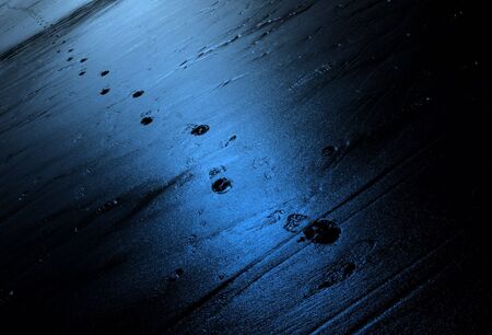Footsteps left in sand on deserted stretch of beach with blue light effectの写真素材