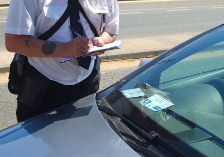 Traffic warden taking details from parked car showing disability permitの写真素材