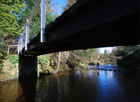 View of bridge and man crossing river using stepping stones