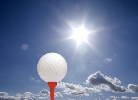 Golf ball on tee with sunflare in cloudy sky