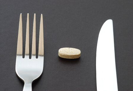 Vitamin pill with knife and fork on textured surfaceの写真素材