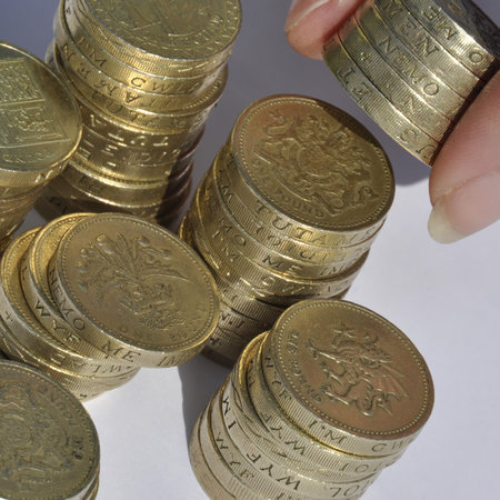 Closeup of stacks of pound coins with hand holding coins.