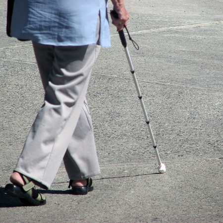 Elderly woman walking in street using walking stickの写真素材