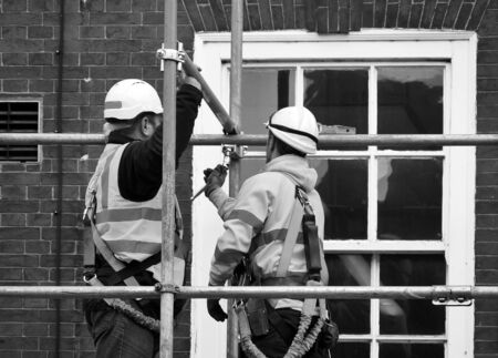 Two workers assembling scaffolding on city buildingの写真素材