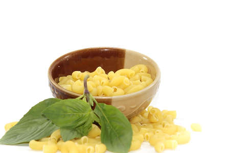Raw macaroni and basil leaves in a plate on a white background.の写真素材