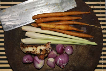 Ingredients - Red Curry Paste - In a white bowl and garlic, shallots, lemongrass, dried chilies, kaffir lime leaves on a traditional home-made wooden cutting board.の写真素材