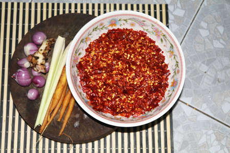 Ingredients - Red Curry Paste - In a white bowl and garlic, shallots, lemongrass, dried chilies, kaffir lime leaves on a traditional home-made wooden cutting board.の写真素材