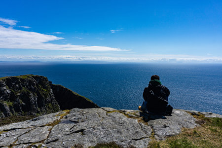 One man standing on the edge of a high cliff with ocean and clouds in the background. Taken in...