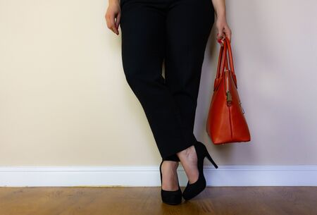 a woman standing with her legs crossed holding on to her bag.の写真素材