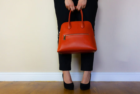 a woman standing with her legs crossed holding on to her bag.