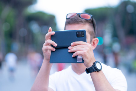 the man in white, takes a selfie on the phone, against the pleasantly blurred background on his tripの写真素材