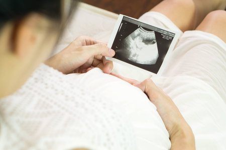Pregnant asian woman looking at ultrasound scan of baby, close up of scan