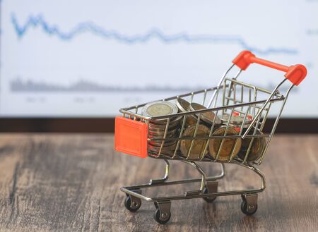 Coin in shopping cart with stock market board background, money for saving and invesment business conceptの写真素材