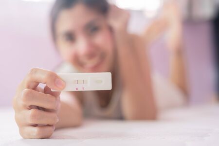 Pregnant asia woman in white dress hole and show a pregnancy test strip with happy and excited, close up of pregnancy test stripの写真素材