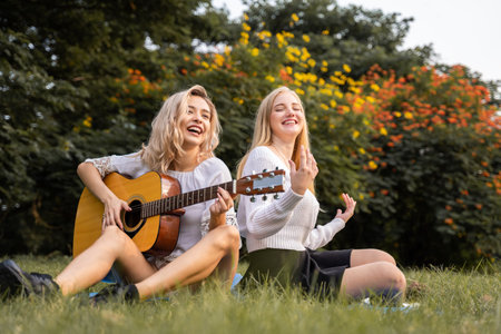 Portrait of caucasian young women sitting in the park outdoor and playing a guitar sing a song together with happinessの写真素材