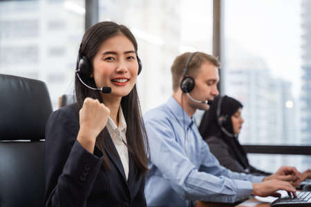 Happy smiling asian woman call center and operator wearing headsets working on computer and talking with customer with her service mindの写真素材
