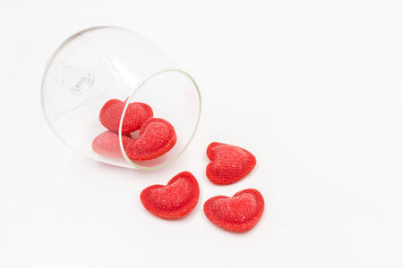 Red heart-shaped sugar sprinkles fall out from a glass on a white background.の写真素材