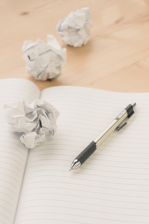 Crumpled paper balls with pen and notebook on wood desk.vintage effect style pictureの写真素材