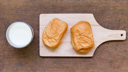 glass of milk and bread on wooden table.