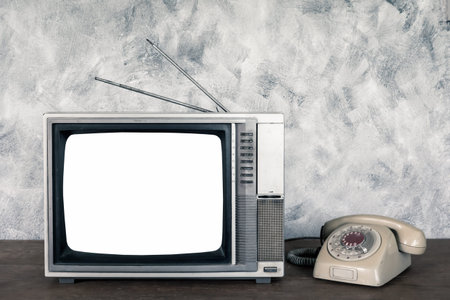 Old analogue television and telephone on wood table with textured background.の写真素材