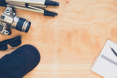 Top view of camera with tripod,hat,glasses and notebook on the wooden table background.の写真素材
