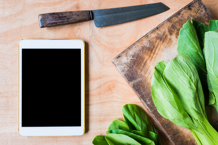 Top view of Bok choy (chinese cabbage) on wooden chopping block with knife and tablet touch computer gadget.の写真素材