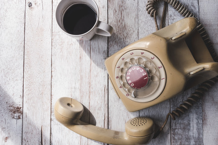 Top view of Old telephone with coffee cup on white wooden table background.の写真素材