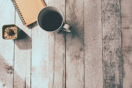 Top view of Coffee cup with notebook and cactus on white wooden table background, Vintage tone, Free space for textの写真素材