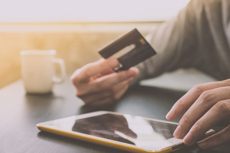 Male hands holding credit card and using Tablet with a cup of coffee on the table, soft focus, flare sun light, Online shopping concept.の写真素材