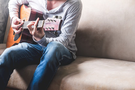 Casual young man playing guitar on sofa at home.