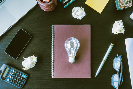 Top view notebook with crumpled paper balls and light bulb on the desk.の写真素材