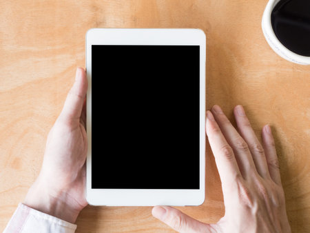 Top view of  male hands using tablet with coffee cup on wooden table.