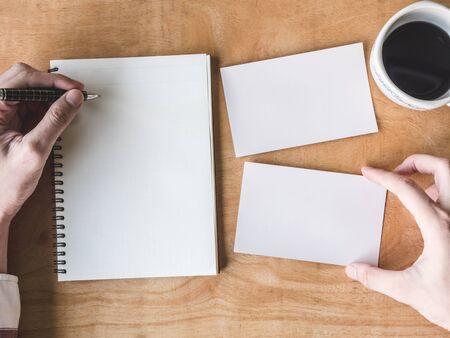 top view of Male hands writing some data in notebook with blank photo cards and coffee cup on wooden table.の写真素材