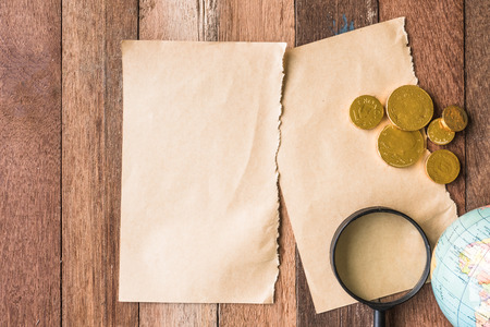 Top view of Blank brown paper with coins, Magnifier and globe on wooden table background.の写真素材